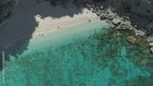 aerial rotating birdview of a loneley hidden beach with three travelers strand aground in the beuty of turquoise water and rocks in it nea cala luna sardinia - drone helicopter shot photo