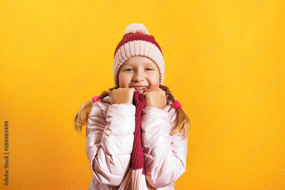 Portrait of a cute little girl in a jacket, scarf and hat on a yellow background. Autumn and winter concept Portrait of a cute little girl in a jacket, scarf and hat on a yellow background. Autumn and winter concept