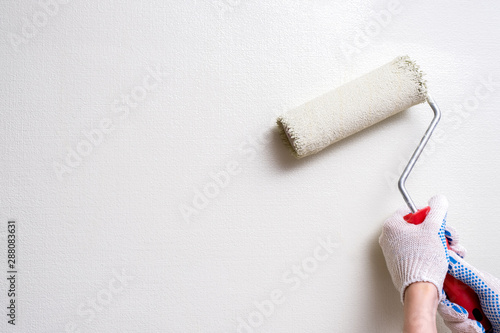 a woman's hand in a construction glove holds a paint roller against a light colored wall