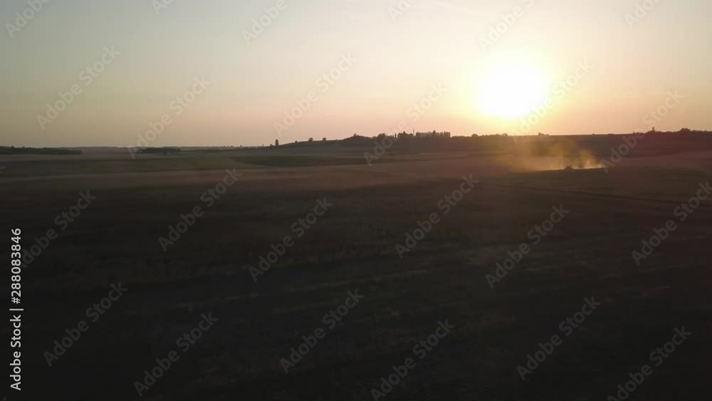 Aerial follow focus upon fields in countryside at sunset with tractor working and volumetric dust. Aerial follow focus upon fields in countryside at sunset with tractor working and volumetric dust.
