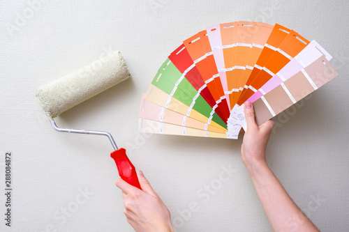 the painter holds the paint roller against the light wall and the color samples. the concept of repair in the apartment and painting the walls