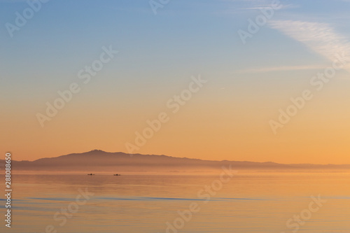 Beautiful view of a lake at sunset, with orange tones and two men on canoes © Massimo