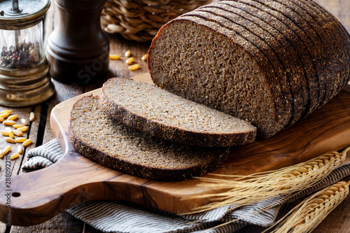 Sliced rye bread on a rustic cutting board with grain and rye ears at the background