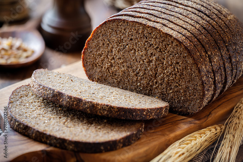 Sliced rye bread on a rustic cutting board with grain and rye ears at the background