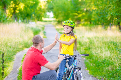 Father and daughter give high five while cycling in the park