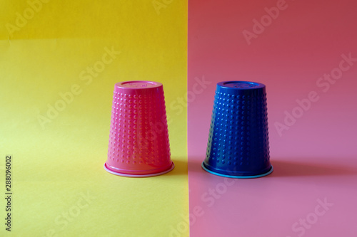 Multi-colored blue and pink plastic cups on a yellow and pink background. Plastic pollution concept.