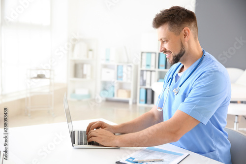 Male nurse working on laptop in clinic