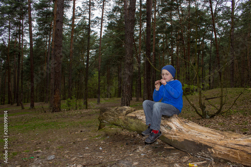boy sitting in forest eating,a little boy alone in the woods dinner sitting on an old tree and eating chocolate