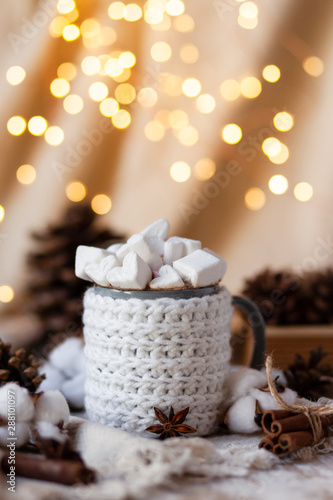 Holiday christmas composition with mug in knitted white sweater with strong hot coffee and marshmallow. Rustic decor, cotton, cones, cinnamon, anise. Lights on. Festive mood, cozy romantic atmosphere