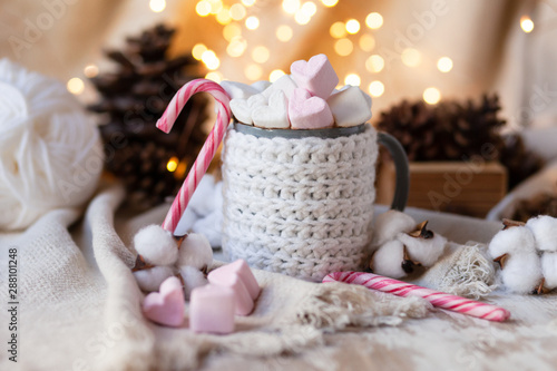 Holiday christmas composition with mug in knitted white sweater with strong hot coffee and marshmallows. Rustic decor, cotton, cones, cinnamon, anise. Lights on. Cozy quite romantic atmosphere