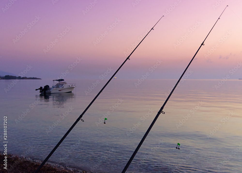 Two fishing rods with bells on fishing line and beautiful beach with boat, at sunrise time.