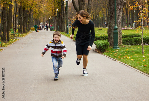 young stylish casual mother with her lovely child son are running in the autumn park and laughing happy. lifestyle sport concept, free space