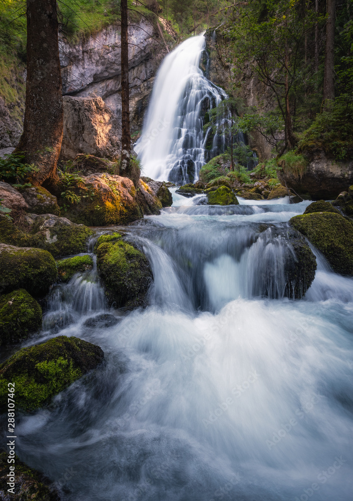 Fototapeta premium Scenic waterfall landscape with green moos stones and flowing river at beautiful summer day in Gollinger, Austria.