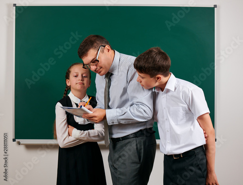 Portrait of a teacher checking homework, reading school exercise books, schoolboy and schoolgirl with old fashioned eyeglasses posing on blackboard background - back to school and education concept photo