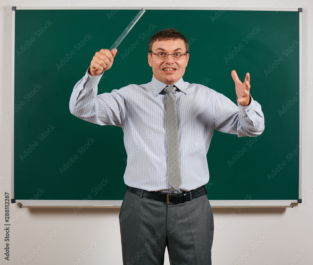 Portrait of a emotional talking man dressed as a school teacher in business suit, posing at blackboard background - learning and education concept