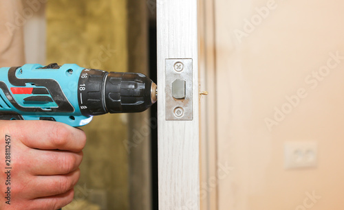 Man is installing the doors handle with a drill. Repair works. Maintenance in the apartment.