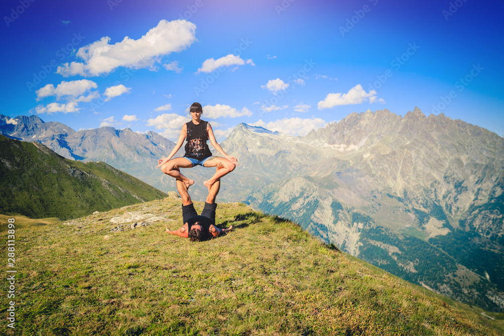Giovane coppia pratica acroyoga e yoga all'aperto in montagna