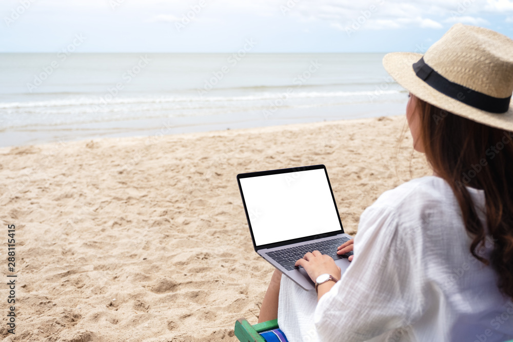 Mockup image of a woman using and typing on laptop computer with blank desktop screen while sitting on a beach chair