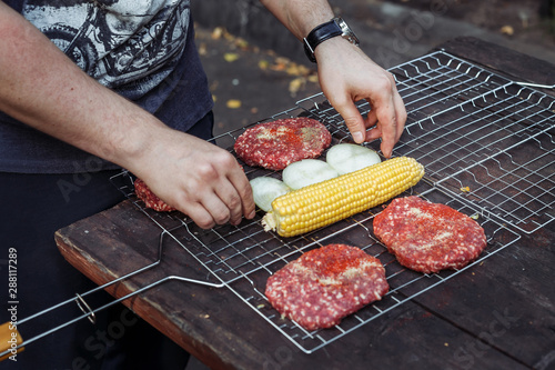 Raw beef cutlets for burger. Popcorn and onion on greel. Men's hands lay grilled vegetables. photo