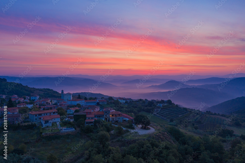 Sunrise in the mountains. The Golden-pink sky, mountains, morning fog and a small village on the mountainside are depicted. Istria, Croatia. The view from the top. Copy space.