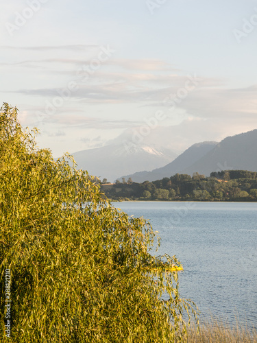 The amazing Choshuenco Volcano surrounded by clouds, over the waters of Lake Panguipulli, in southern Chile. photo