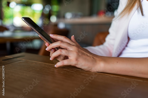 Closeup shot of young woman chatting with family at social networks, woman hands using smartphone indoor, lifestyle and communication concept. Hand of woman using smartphone on wooden table