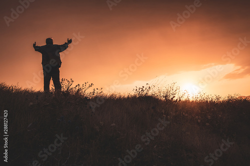 silhouette of a mediating man on top of mountain in sunset  doing magic  a majestical scene 