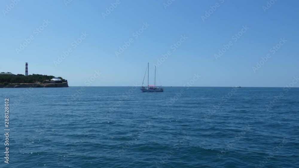 Yacht moving fast to camera, view from ship. Sea coast with lighthouse and forest at the back. Sunny summer day. Travel theme. Yacht moving fast to camera, view from ship. Sea coast with lighthouse and forest at the back. Sunny summer day. Travel theme.