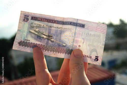 A man holding 5 saudi riyal in his hand. Saudi Arabia currency. photo