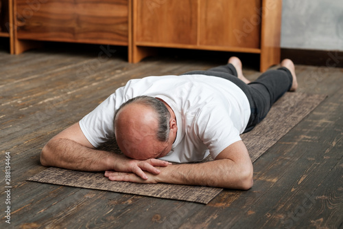 Senior aged man resting after yoga exercise on floor. Sports at home for health. Restorative posture.