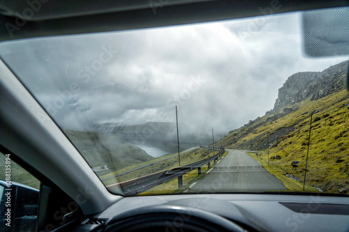 Driver's perspective from the inside of a car during a road trip through snow-covered valleys on the Faroe Islands.