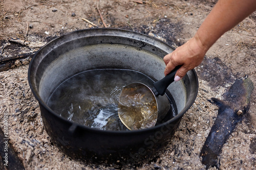 Boiling water in cauldron. Woman's hand taking water in cauldron with a kettle for cooking in the forest.