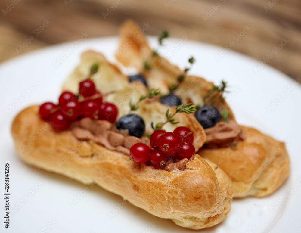 eclairs decorated with fresh berries on a white plate, handmade, culinary theme, close up