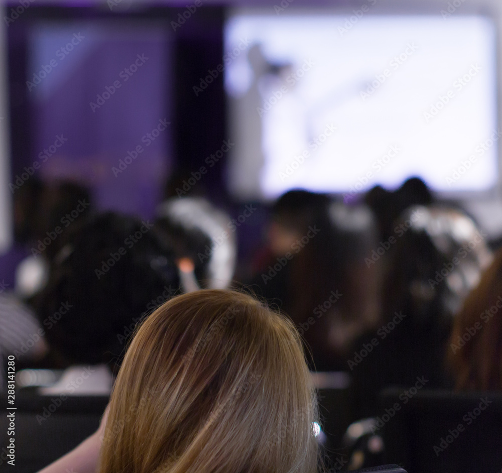 Speaker with hand up in front of audience in conference hall. Corporate executive manager giving speech during business seminar. Presenter giving presentation at executive leadership workshop. 