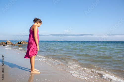 teenage girl standing by the seashore looking sad and lonely