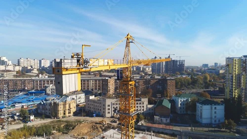 High building construction site. Big industrial tower crane with blue sky amd cityscape on background. Concrete plates weight balance. Counterweight. Aerial drone view. Metropolis city development.