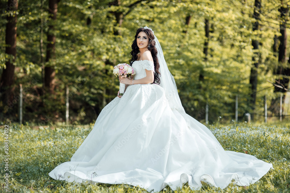 Young beautiful stylish woman, bride, bridal fashion, spring trend, flowers, roses, hairstyle, beauty make-up, white dress. Wedding day. Happy bride in a beautiful dress walking in the park