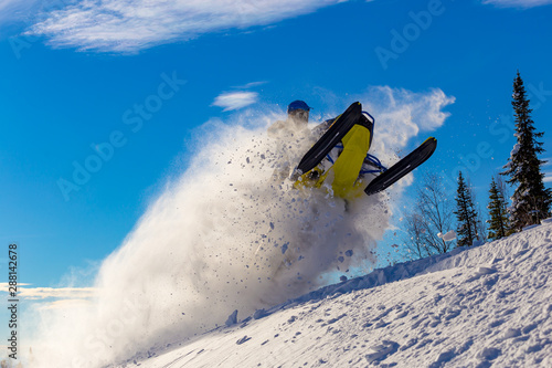 snowmobile jump. bright snowmobile in motion. the guy is flying on a snowmobile on a background of blue sky leaving a trail of splashes of white snow. bright snowmobile and suit without brands. super