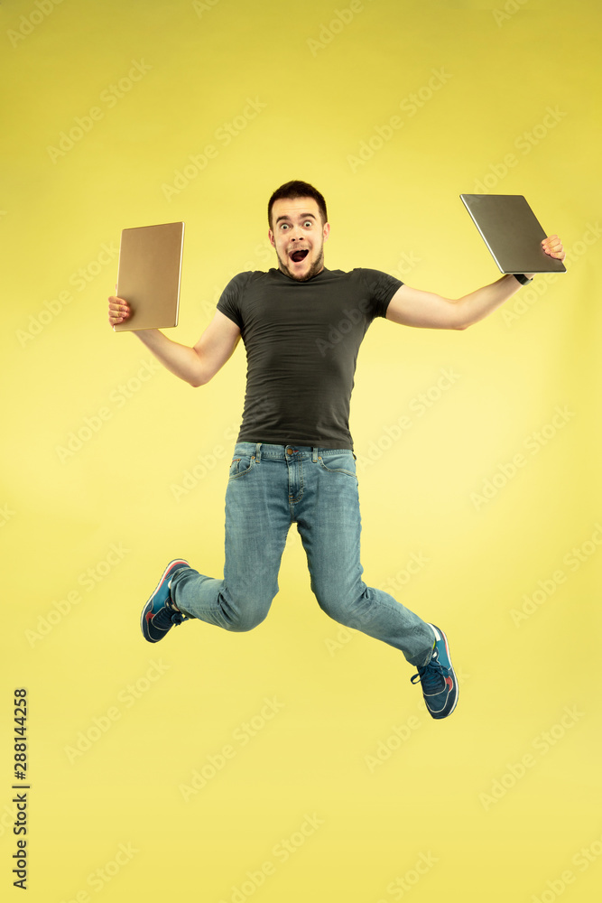 Weightless. Full length portrait of happy jumping man with gadgets isolated on yellow background. Modern tech, freedom of choices concept, emotions concept. Using tablet for selfie or vlog in flight. Weightless. Full length portrait of happy jumping man with gadgets isolated on yellow background. Modern tech, freedom of choices concept, emotions concept. Using tablet for selfie or vlog in flight.