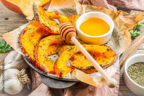 Autumn vegetarian food recipe. Organic roasted vegetables, Baked fried Hokkaido pumpkin with olive oil, herbs, garlic and honey. On wooden rustic background, copy space