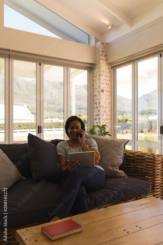 Woman talking on mobile phone while using digital tablet in living room Woman talking on mobile phone while using digital tablet in living room