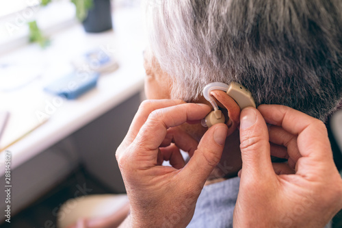Slika na platnu Male doctor applying hearing aid to senior woman