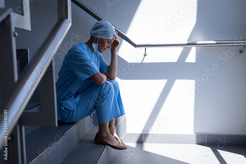 Upset female surgeon sitting on stair case in hospital