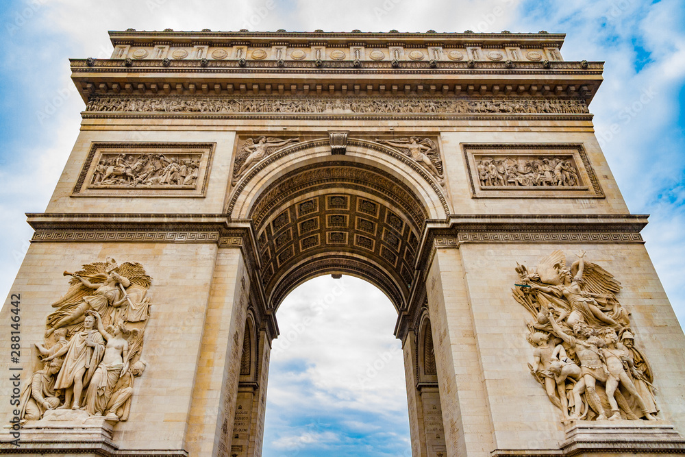 Great low angle shot of the stately Arc de Triomphe seen from the east with the two sculptures Le Départ and Le Triomphe with a dramatic blue sky. It is one of the most famous monuments in Paris.