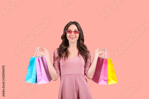 Black friday season sale concept. Attractive young woman with long brunette hair, wearing tight dress, holding many different blank shopping bags over pink isolated background. Copy space, close up