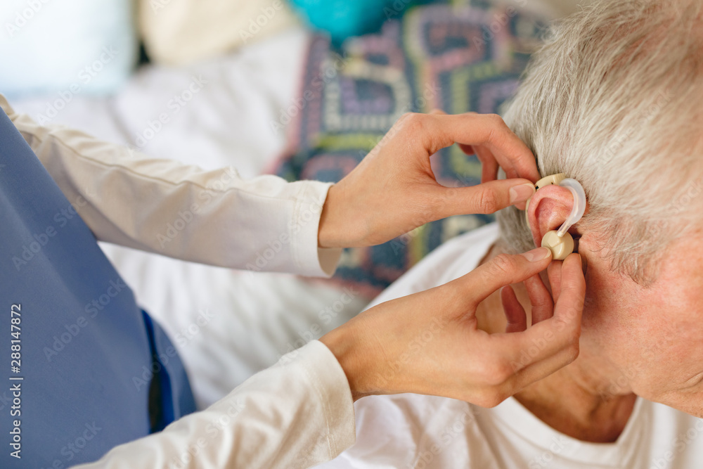 Female nurse applying hearing aid to senior male patient ear Female nurse applying hearing aid to senior male patient ear