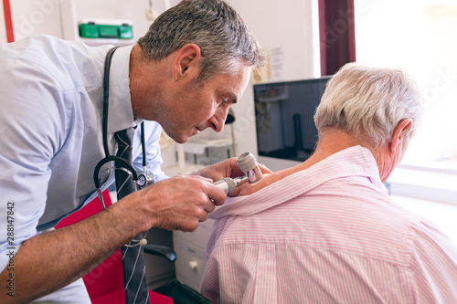 Male dermatologist examining senior patient with dermatoscopy