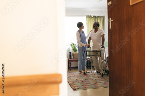 Female nurse talking with senior man while walking with walker 