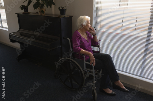 Side view of disabled senior woman sitting on wheelchair and looking outside through window