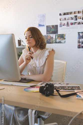Female graphic designer working on graphics tablet and computer at desk